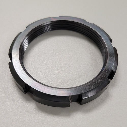 A round metal locknut with machined slots and internal threading, displayed on a grey background.