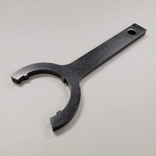 A black wrench tool with a rounded opening and flat handle, designed for a specific application, lying on a grey surface.