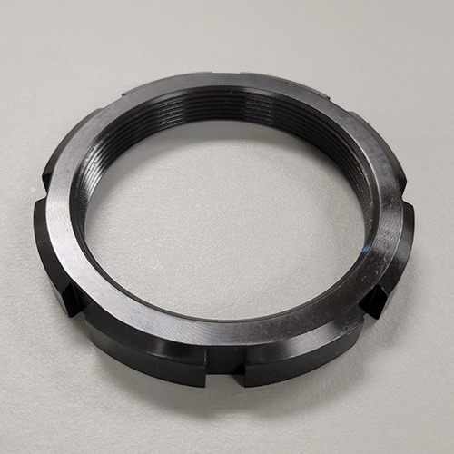 A round metal locknut with machined slots and internal threading, displayed on a grey background.