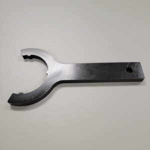 A black wrench tool with a rounded opening and flat handle, designed for a specific application, lying on a grey surface.