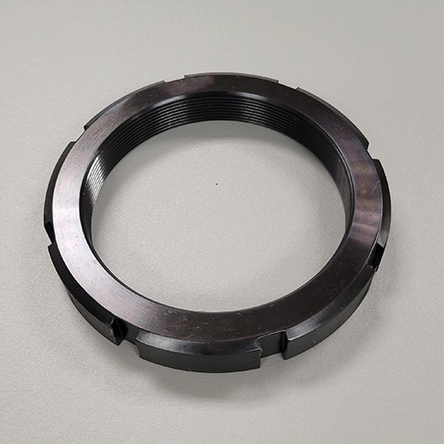 A round metal locknut with machined slots and internal threading, displayed on a grey background.