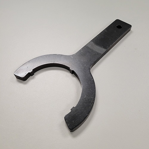 A black wrench tool with a rounded opening and flat handle, designed for a specific application, lying on a grey surface.