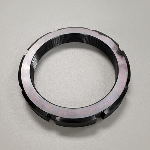 A round metal locknut with machined slots and internal threading, displayed on a grey background.