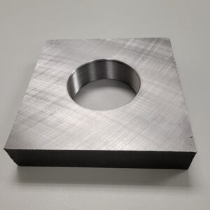 A square metal plate with a threaded central hole, resting on a rough concrete surface.