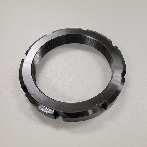 A round metal locknut with machined slots and internal threading, displayed on a grey background.