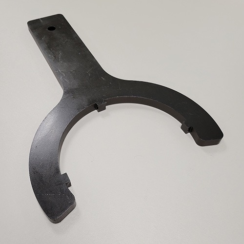 A black wrench tool with a rounded opening and flat handle, designed for a specific application, lying on a grey surface.