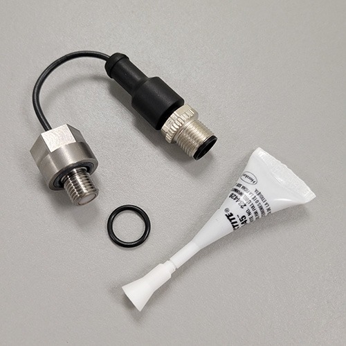 An industrial sensor with a black cable and metal threaded connector, a separate metallic nut, a rubber O-ring, and a tube of thread sealant on a grey surface.