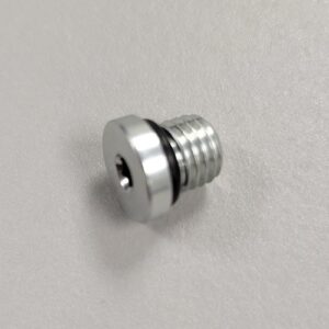 Close-up of a metallic hex-head threaded plug with an internal hexagonal recess, on a plain white background.