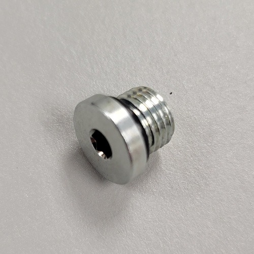 Close-up of a metallic hex-head threaded plug with an internal hexagonal recess, on a plain white background.