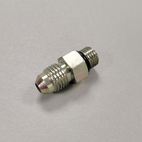 Metallic hydraulic connector with a hex nut in the center and threaded ends, lying on a white surface