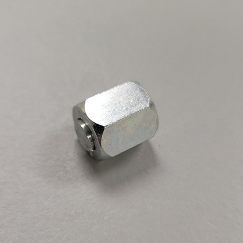 A silver hexagonal nylock nut with a nylon insert visible from the side, placed on a grey surface