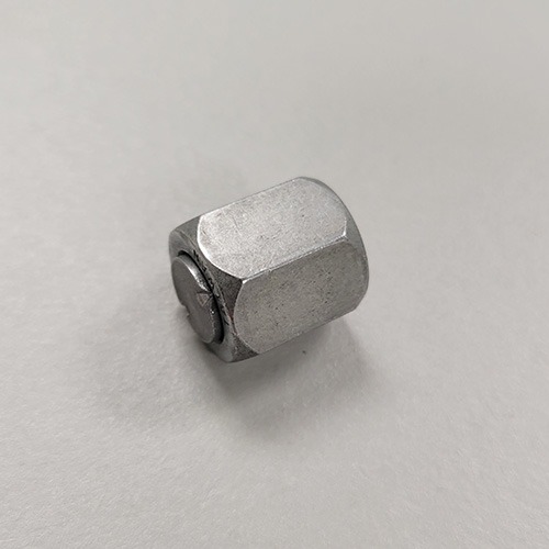 A silver hexagonal nylock nut with a nylon insert visible from the side, placed on a white surface
